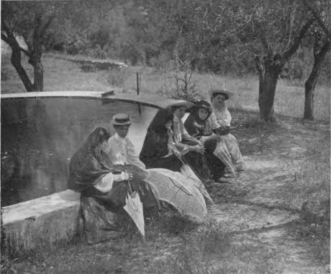 There are six ladies in
this photo, arranged informally seated on one side of a short stone wall that
appears to surround a small pool of water, with several trees in the
background. Three of the ladies are dressed in light colored Western attire
that completely covers their bodies, with light-colored brimmed hats.
The other three ladies are in dark robes with attached head coverings.
These three are holding folded umbrellas with their hands. The three in dark
attire appear to be of late teen or early adult age, with the other three
appearing to be somewhat older.