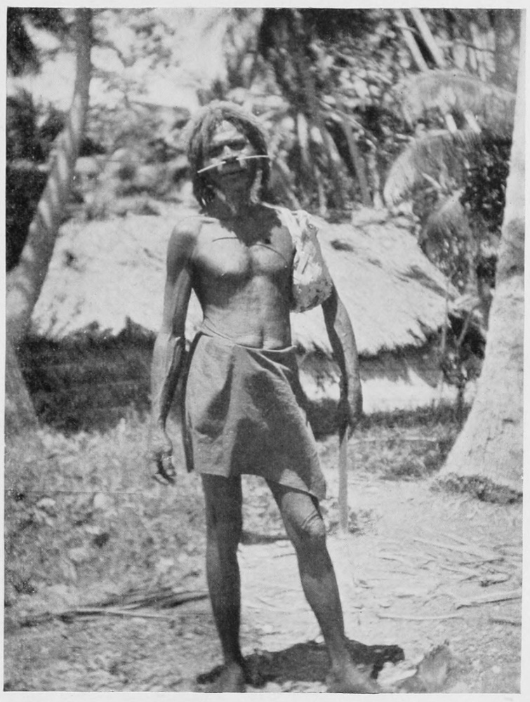 Young well-proportioned, adult male wearing a loincloth, with a long piece of bone threaded through his nostrils, poses towards the viewer